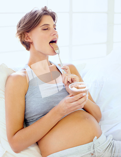Image of Relax, pregnant and a woman eating pudding on a sofa in the living room of her home for hunger craving. Happy, food or chocolate dessert with a young mother in her apartment for pregnancy growth