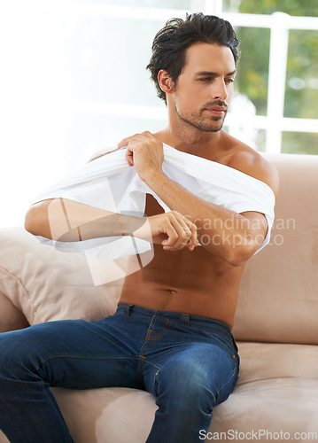 Image of Take off, tshirt and man on sofa in a house for comfort, rest or chilling on weekend, day off or vacation. Sweater, removal or male person in living room undressing, relax and ready to be comfortable