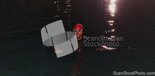 Image of A determined professional triathlete undergoes rigorous night time training in cold waters, showcasing dedication and resilience in preparation for an upcoming triathlon swim competition