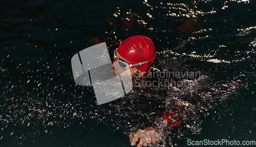 Image of A determined professional triathlete undergoes rigorous night time training in cold waters, showcasing dedication and resilience in preparation for an upcoming triathlon swim competition