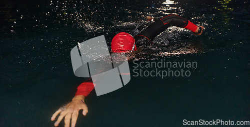 Image of A determined professional triathlete undergoes rigorous night time training in cold waters, showcasing dedication and resilience in preparation for an upcoming triathlon swim competition