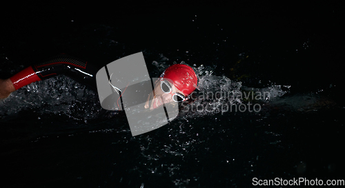 Image of A determined professional triathlete undergoes rigorous night time training in cold waters, showcasing dedication and resilience in preparation for an upcoming triathlon swim competition