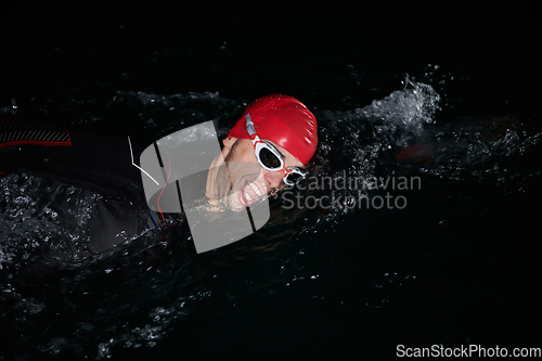 Image of A determined professional triathlete undergoes rigorous night time training in cold waters, showcasing dedication and resilience in preparation for an upcoming triathlon swim competition