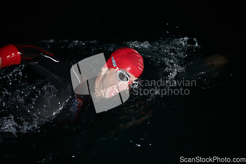 Image of A determined professional triathlete undergoes rigorous night time training in cold waters, showcasing dedication and resilience in preparation for an upcoming triathlon swim competition