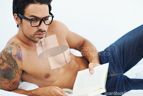 Image of Relax, glasses and a shirtless man reading a book in the bedroom of his apartment for hobby or leisure. Thinking, storytelling and the body of an intelligent young person lying on the bed of his home