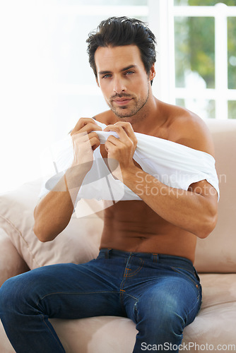 Image of Portrait, body and a young man dressing on a sofa in the living room of his home for fashion in the morning. Clothes, style and confident with a shirtless young person getting ready in an apartment