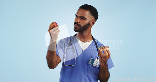 Image of Doctor, apple and donut for health, diet or natural nutrition against a blue studio background. Man, medical nurse or surgeon with organic fruit and dessert in choice for wellness on mockup space