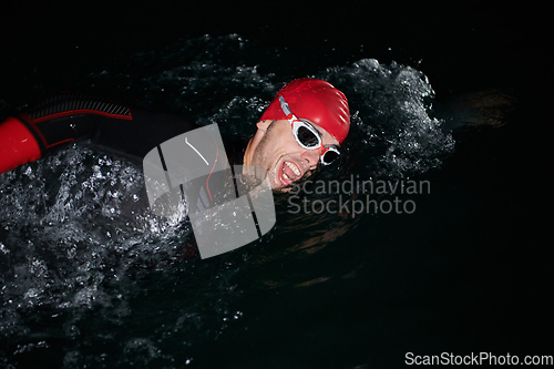 Image of A determined professional triathlete undergoes rigorous night time training in cold waters, showcasing dedication and resilience in preparation for an upcoming triathlon swim competition