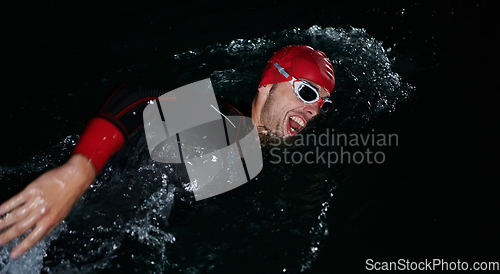 Image of A determined professional triathlete undergoes rigorous night time training in cold waters, showcasing dedication and resilience in preparation for an upcoming triathlon swim competition