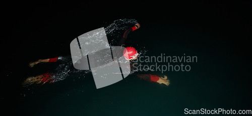 Image of A determined professional triathlete undergoes rigorous night time training in cold waters, showcasing dedication and resilience in preparation for an upcoming triathlon swim competition