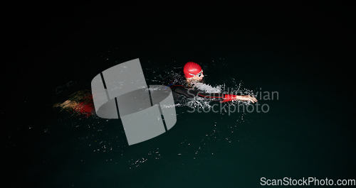 Image of A determined professional triathlete undergoes rigorous night time training in cold waters, showcasing dedication and resilience in preparation for an upcoming triathlon swim competition