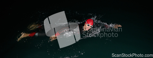 Image of A determined professional triathlete undergoes rigorous night time training in cold waters, showcasing dedication and resilience in preparation for an upcoming triathlon swim competition