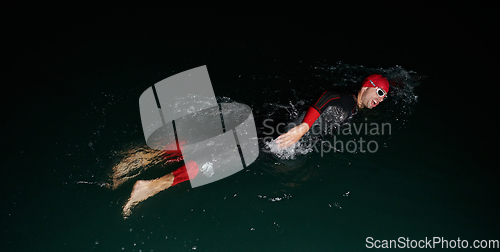 Image of A determined professional triathlete undergoes rigorous night time training in cold waters, showcasing dedication and resilience in preparation for an upcoming triathlon swim competition