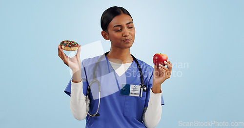 Image of Apple, donut and nurse in studio with choice for healthy eating, diet and detox on blue background. Thinking, healthcare and Indian woman with dessert, fruit and cake for decision, option and balance