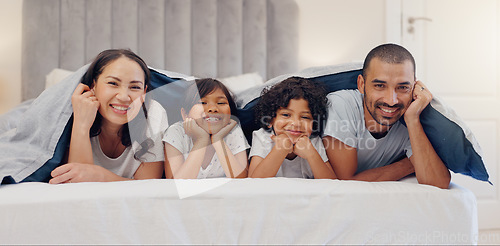 Image of Portrait, smile and children with parents in bed relaxing and bonding together at family home. Happy, fun and young mother and father laying and resting with kids in bedroom of modern house.