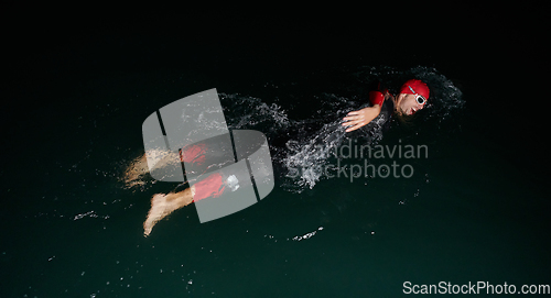 Image of A determined professional triathlete undergoes rigorous night time training in cold waters, showcasing dedication and resilience in preparation for an upcoming triathlon swim competition