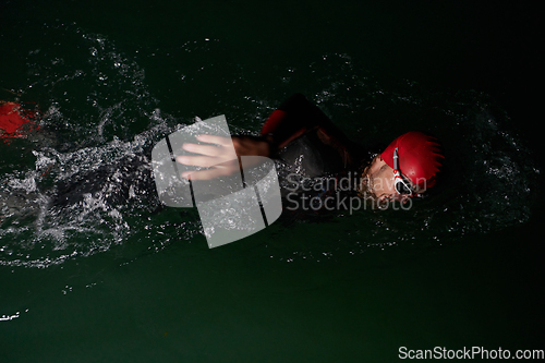 Image of A determined professional triathlete undergoes rigorous night time training in cold waters, showcasing dedication and resilience in preparation for an upcoming triathlon swim competition