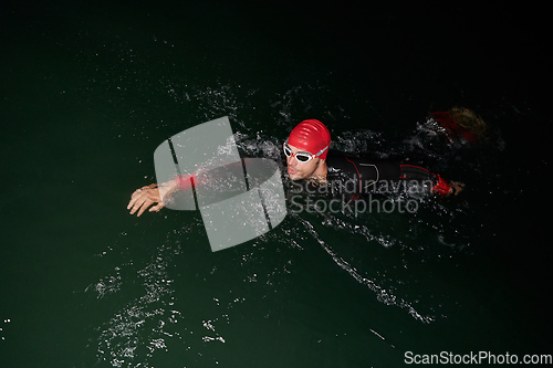 Image of A determined professional triathlete undergoes rigorous night time training in cold waters, showcasing dedication and resilience in preparation for an upcoming triathlon swim competition