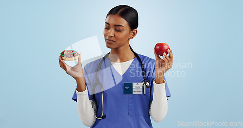 Image of Apple, donut and doctor in studio with choice for healthy eating, diet and detox on blue background. Thinking, healthcare and Indian woman with candy, fruit and cake for decision, diabetes or balance