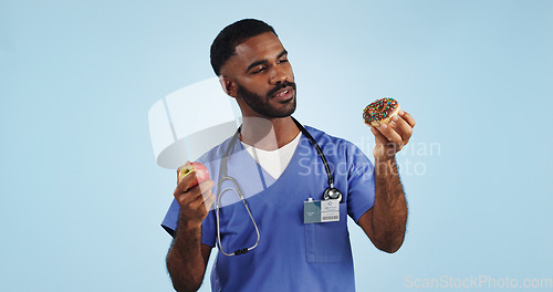 Image of Doctor, man and studio for donut, apple and choice with thinking for healthcare by blue background. Medic, person or nutritionist with decision, cake and fruit with ideas for food, eating and diet