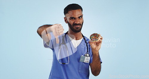 Image of Man, portrait and doctor with thumbs down, donut or bad review for diet against a blue studio background. Brazilian person or medical nurse rejection, no emoji or sign for chocolate dessert on mockup