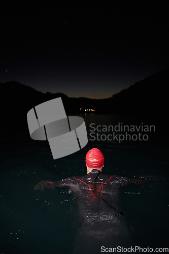 Image of A determined professional triathlete undergoes rigorous night time training in cold waters, showcasing dedication and resilience in preparation for an upcoming triathlon swim competition