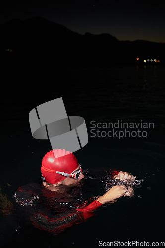 Image of A determined professional triathlete undergoes rigorous night time training in cold waters, showcasing dedication and resilience in preparation for an upcoming triathlon swim competition