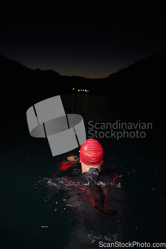 Image of A determined professional triathlete undergoes rigorous night time training in cold waters, showcasing dedication and resilience in preparation for an upcoming triathlon swim competition