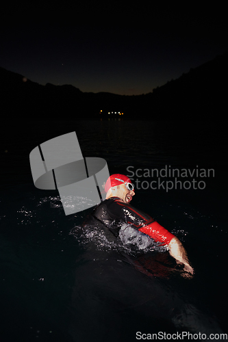 Image of A determined professional triathlete undergoes rigorous night time training in cold waters, showcasing dedication and resilience in preparation for an upcoming triathlon swim competition