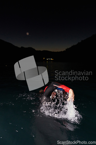 Image of A determined professional triathlete undergoes rigorous night time training in cold waters, showcasing dedication and resilience in preparation for an upcoming triathlon swim competition