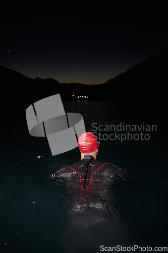 Image of A determined professional triathlete undergoes rigorous night time training in cold waters, showcasing dedication and resilience in preparation for an upcoming triathlon swim competition