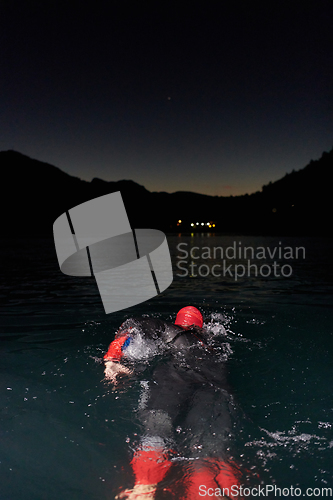 Image of A determined professional triathlete undergoes rigorous night time training in cold waters, showcasing dedication and resilience in preparation for an upcoming triathlon swim competition