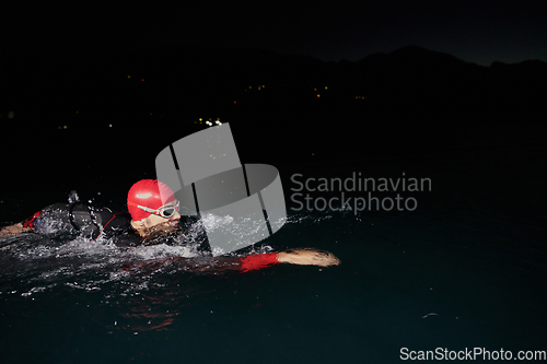 Image of A determined professional triathlete undergoes rigorous night time training in cold waters, showcasing dedication and resilience in preparation for an upcoming triathlon swim competition