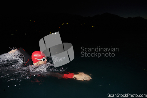 Image of A determined professional triathlete undergoes rigorous night time training in cold waters, showcasing dedication and resilience in preparation for an upcoming triathlon swim competition