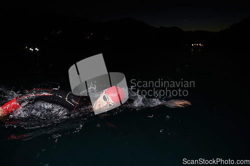 Image of A determined professional triathlete undergoes rigorous night time training in cold waters, showcasing dedication and resilience in preparation for an upcoming triathlon swim competition