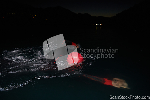 Image of A determined professional triathlete undergoes rigorous night time training in cold waters, showcasing dedication and resilience in preparation for an upcoming triathlon swim competition