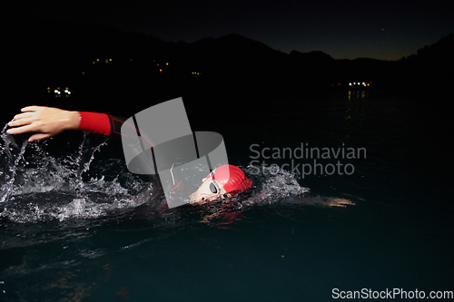 Image of A determined professional triathlete undergoes rigorous night time training in cold waters, showcasing dedication and resilience in preparation for an upcoming triathlon swim competition