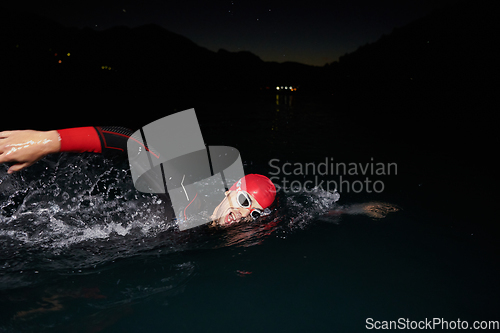 Image of A determined professional triathlete undergoes rigorous night time training in cold waters, showcasing dedication and resilience in preparation for an upcoming triathlon swim competition