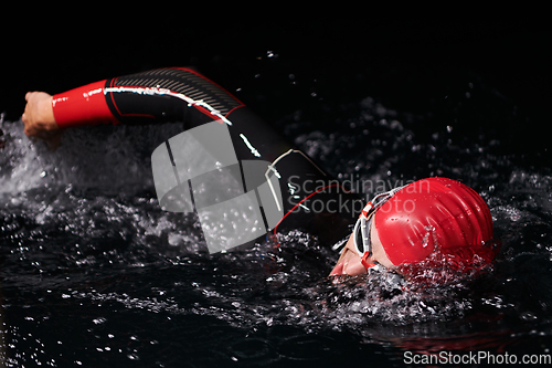 Image of A determined professional triathlete undergoes rigorous night time training in cold waters, showcasing dedication and resilience in preparation for an upcoming triathlon swim competition