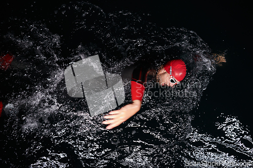 Image of A determined professional triathlete undergoes rigorous night time training in cold waters, showcasing dedication and resilience in preparation for an upcoming triathlon swim competition