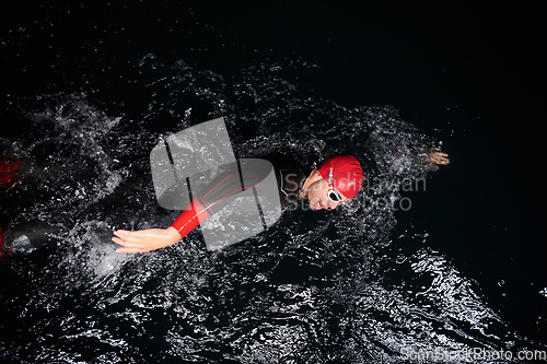 Image of A determined professional triathlete undergoes rigorous night time training in cold waters, showcasing dedication and resilience in preparation for an upcoming triathlon swim competition