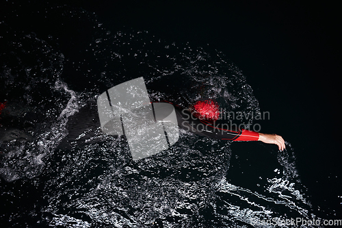 Image of A determined professional triathlete undergoes rigorous night time training in cold waters, showcasing dedication and resilience in preparation for an upcoming triathlon swim competition