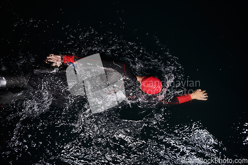 Image of A determined professional triathlete undergoes rigorous night time training in cold waters, showcasing dedication and resilience in preparation for an upcoming triathlon swim competition