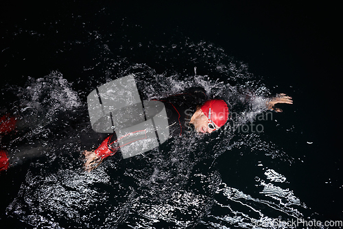 Image of A determined professional triathlete undergoes rigorous night time training in cold waters, showcasing dedication and resilience in preparation for an upcoming triathlon swim competition