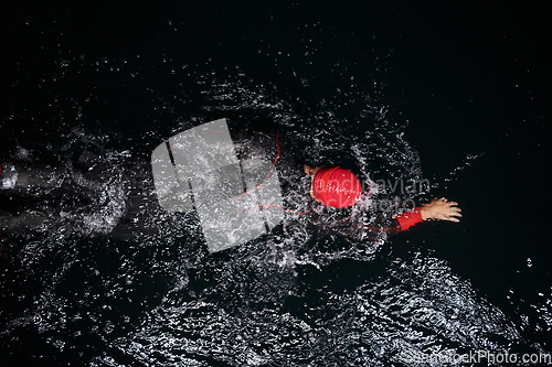 Image of A determined professional triathlete undergoes rigorous night time training in cold waters, showcasing dedication and resilience in preparation for an upcoming triathlon swim competition