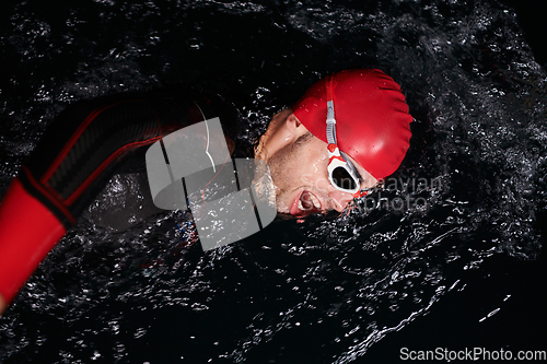 Image of A determined professional triathlete undergoes rigorous night time training in cold waters, showcasing dedication and resilience in preparation for an upcoming triathlon swim competition