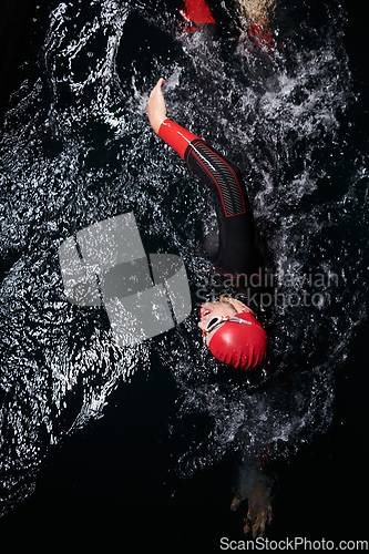 Image of A determined professional triathlete undergoes rigorous night time training in cold waters, showcasing dedication and resilience in preparation for an upcoming triathlon swim competition