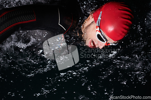 Image of A determined professional triathlete undergoes rigorous night time training in cold waters, showcasing dedication and resilience in preparation for an upcoming triathlon swim competition