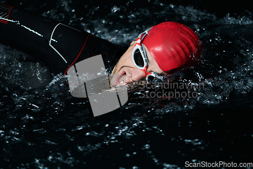 Image of A determined professional triathlete undergoes rigorous night time training in cold waters, showcasing dedication and resilience in preparation for an upcoming triathlon swim competition