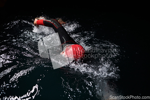 Image of A determined professional triathlete undergoes rigorous night time training in cold waters, showcasing dedication and resilience in preparation for an upcoming triathlon swim competition